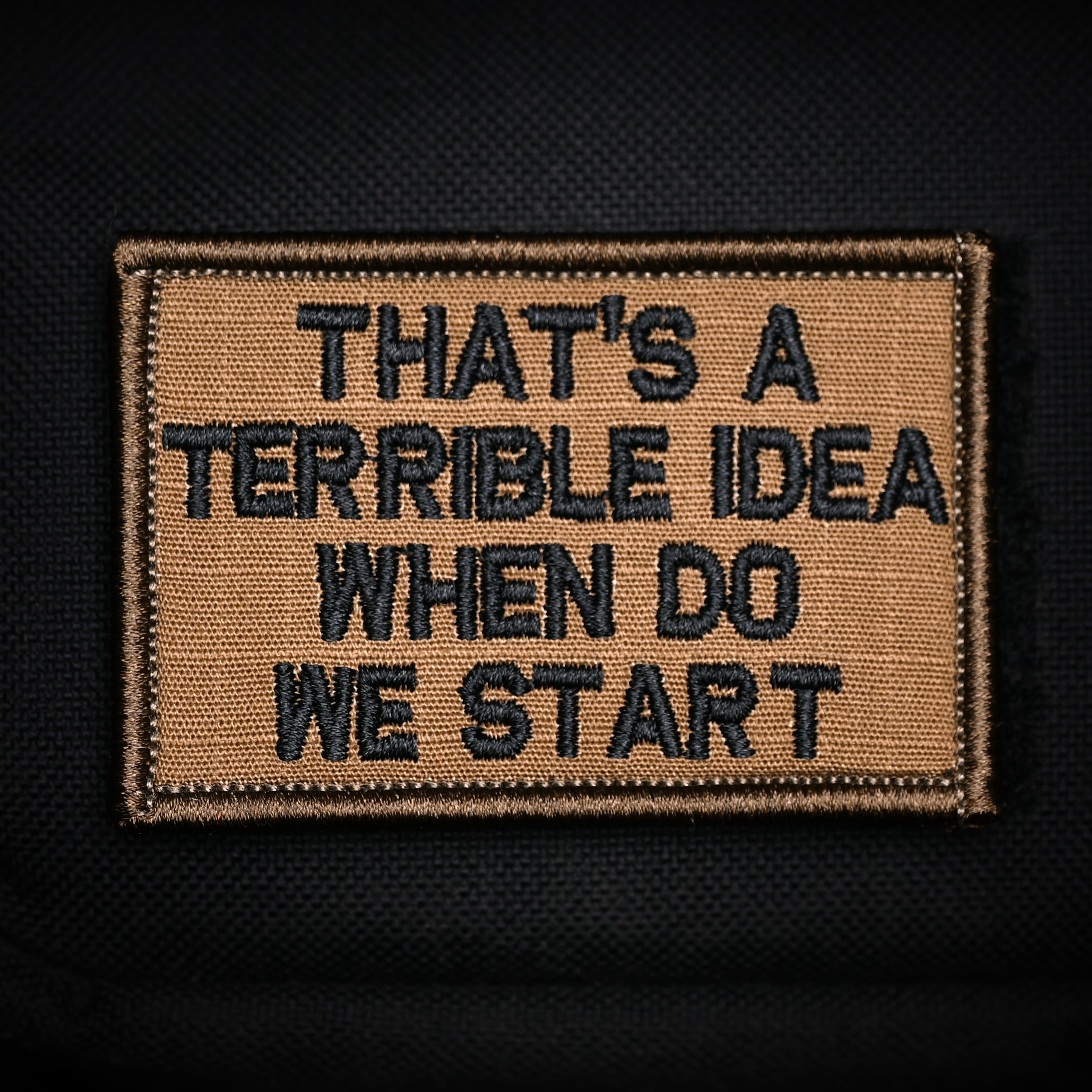 A rectangular velcro patch with a brown background and black text that reads 'THAT'S A TERRIBLE IDEA WHEN DO WE START?'