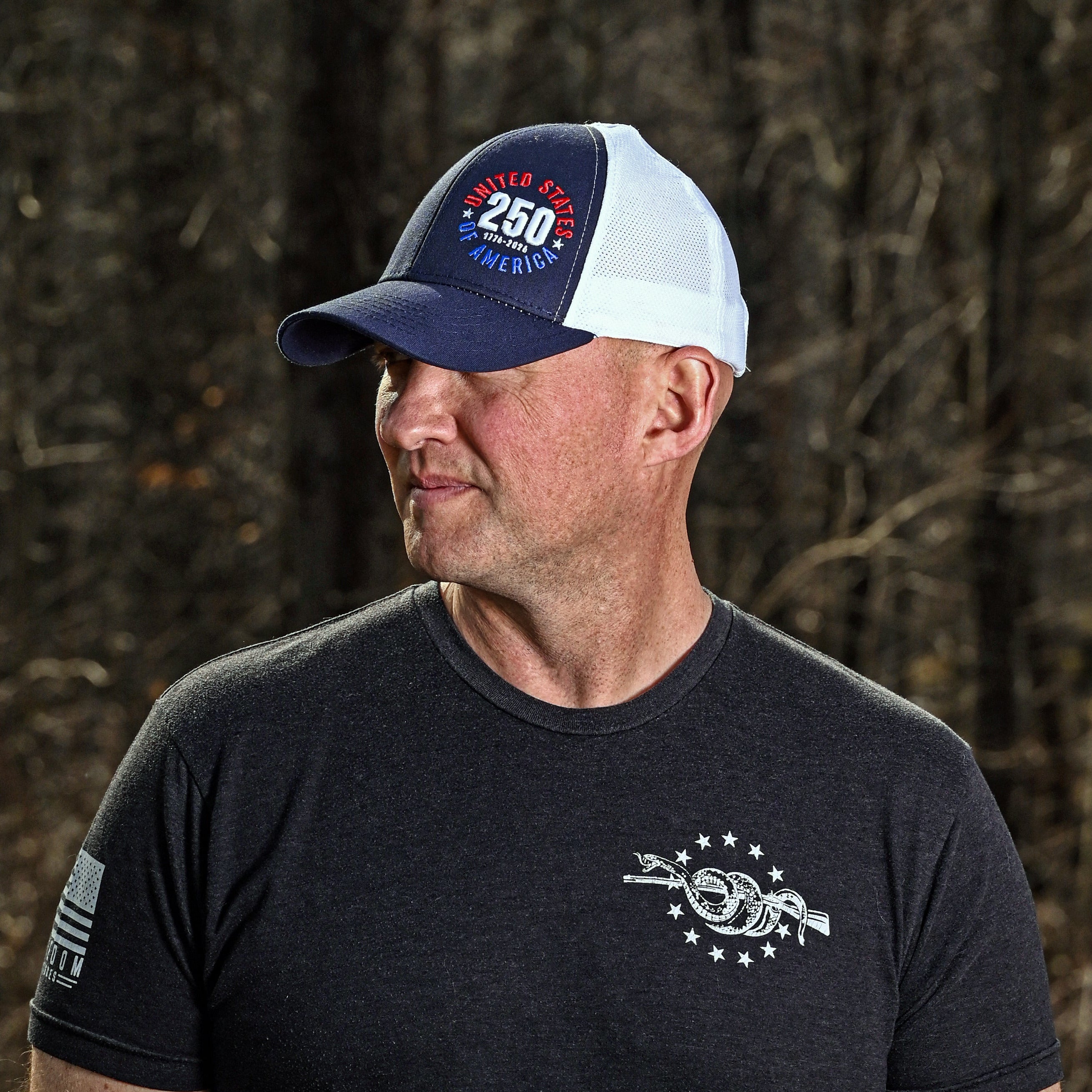 Man wearing a cap and black t-shirt with a logo against a natural background