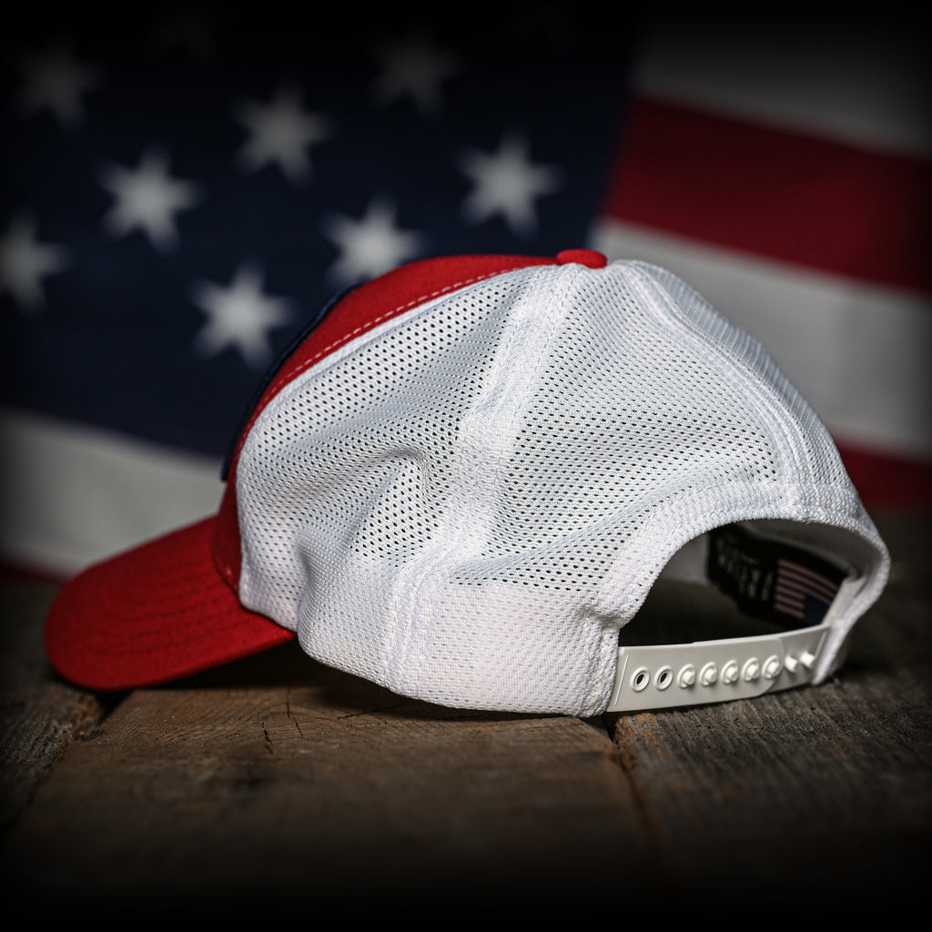 Red and white trucker hat on a wooden surface with an American flag in the background