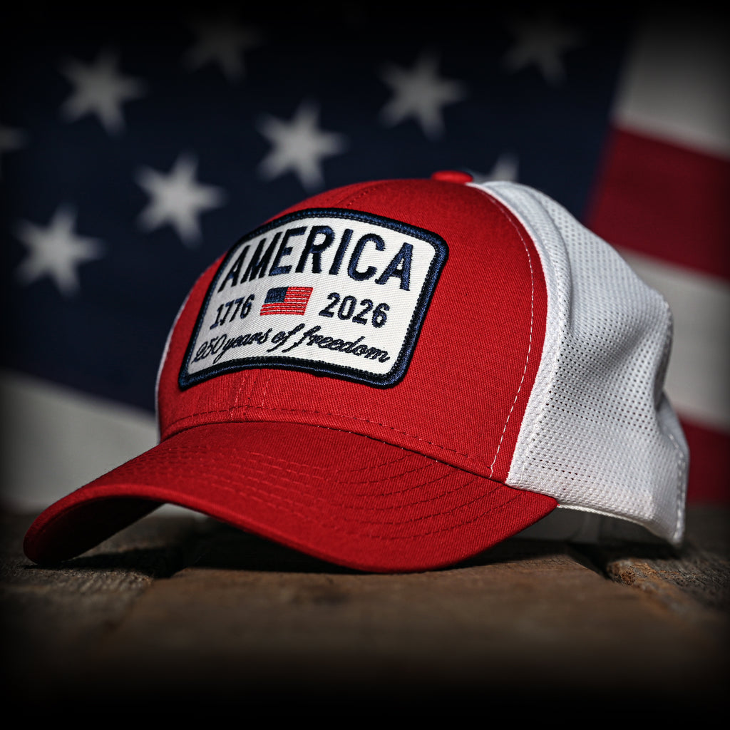 Red and white cap with 'America 1776-2026' patch in front of an American flag.