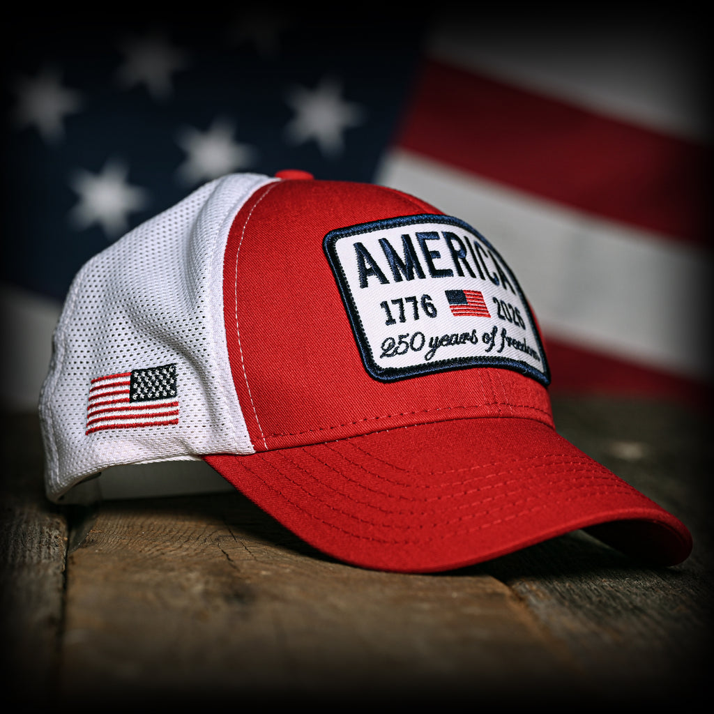 Red and white trucker hat with 'America 250 years of freedom' patch in front of an American flag