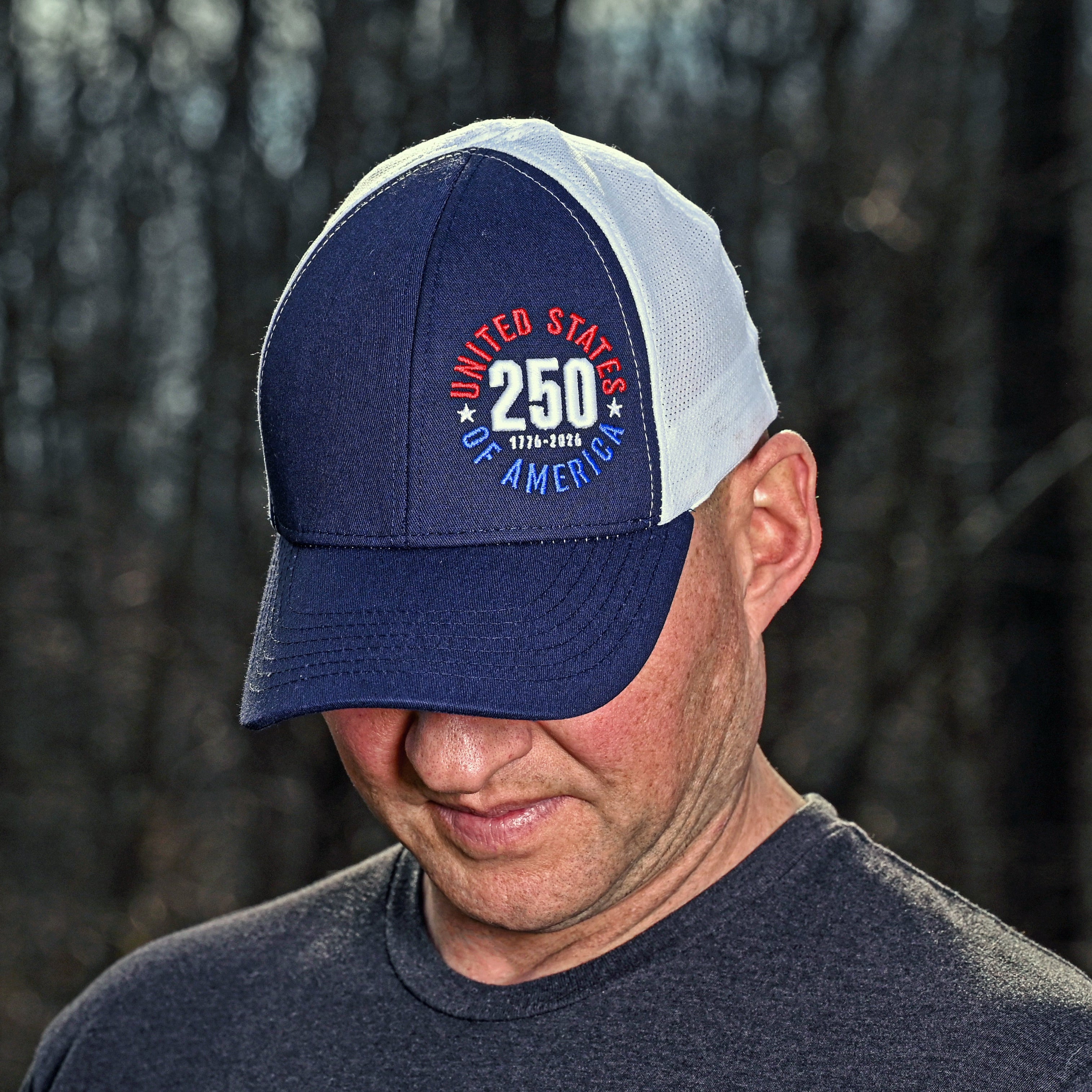 Man wearing a blue and white cap with 'United States of America 250' text against a dark background