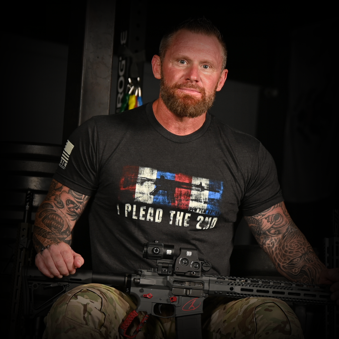 Cash Care wearing a black t-shirt with a graphic design, holding a rifle in a dark setting