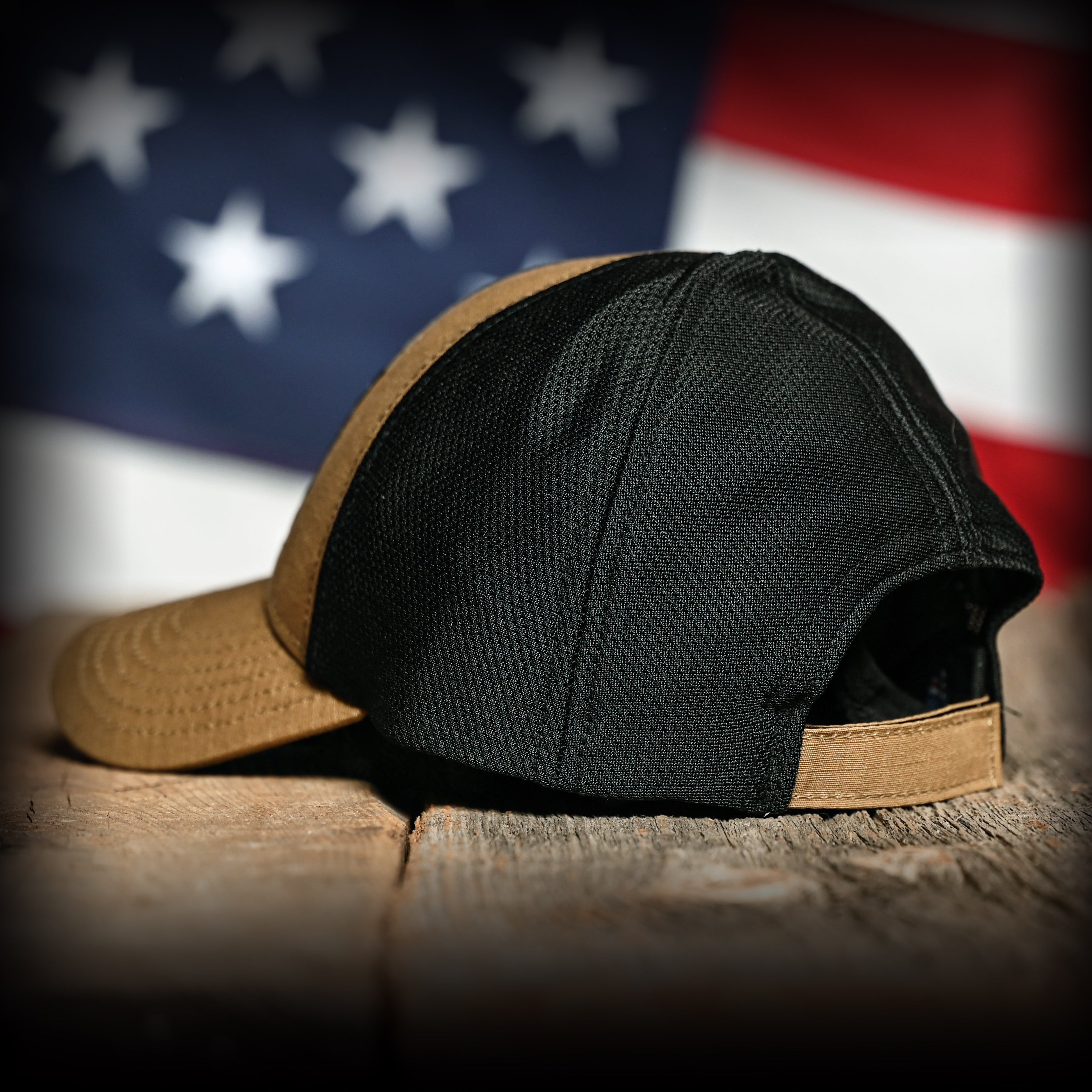 Coyote brown cap with black mesh on a wooden surface in front of an American flag
