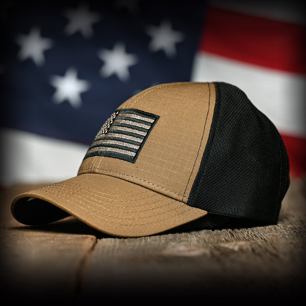 Coyote brown and black mesh cap with an embroidered flag on a wooden surface with an American flag in the background