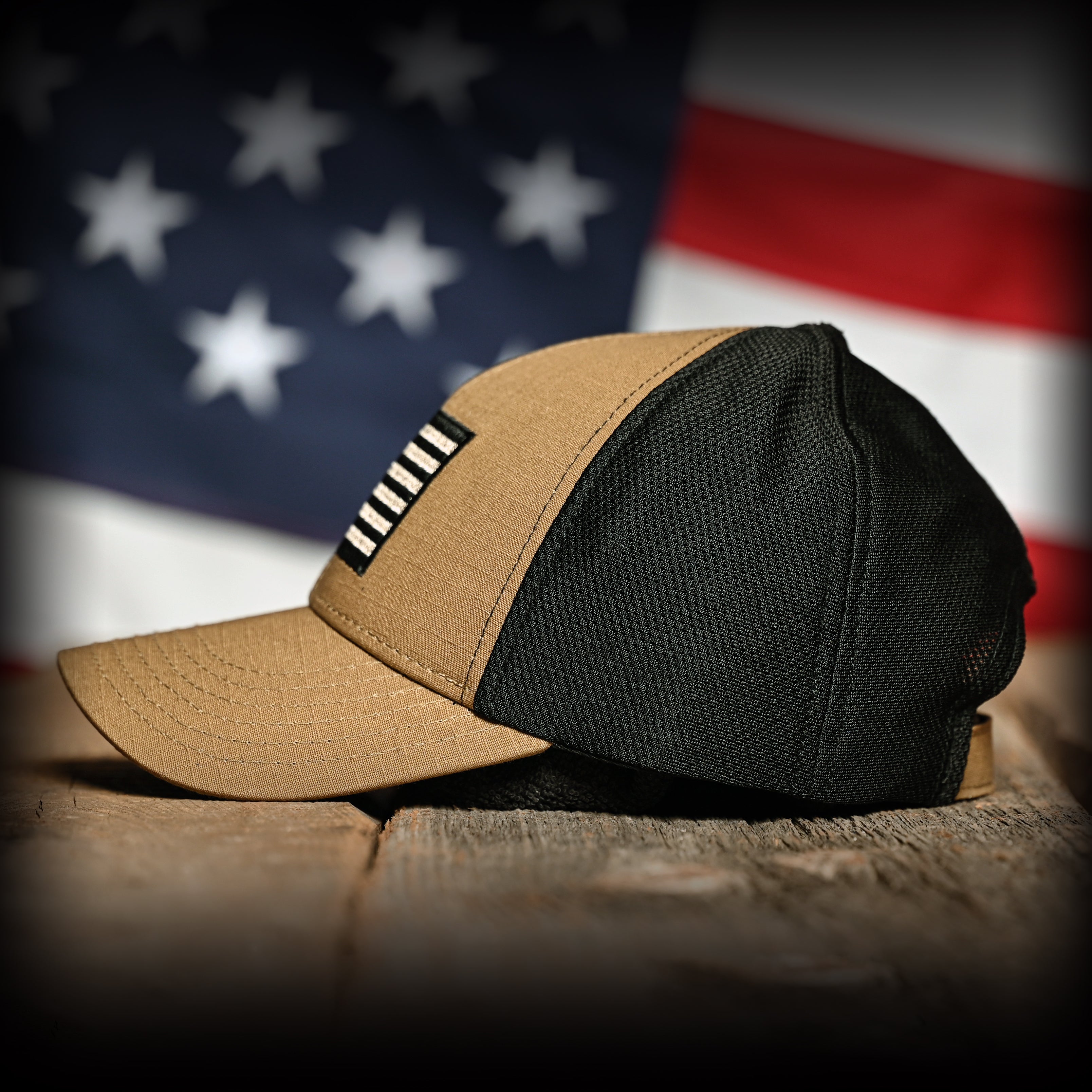Left side view of the coyote brown and black hat on a wooden surface with an American flag in the background.