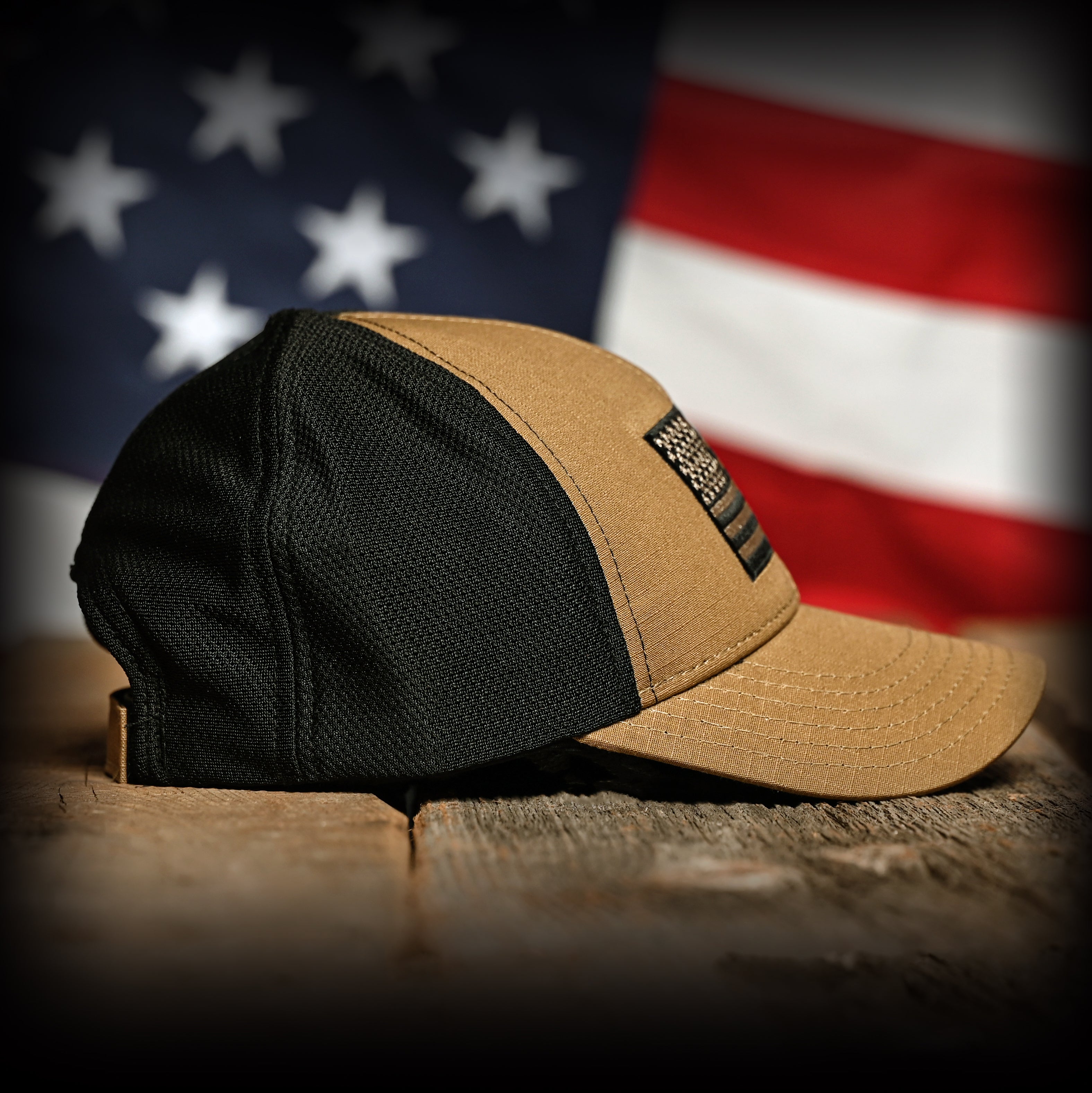 Right side of a coyote brown and black hat on a wooden surface with an American flag in the background