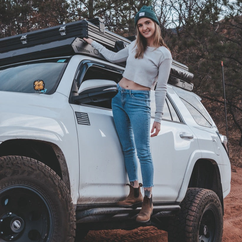 Woman standing next to a white SUV with an American flag vehicle magnet in a natural setting