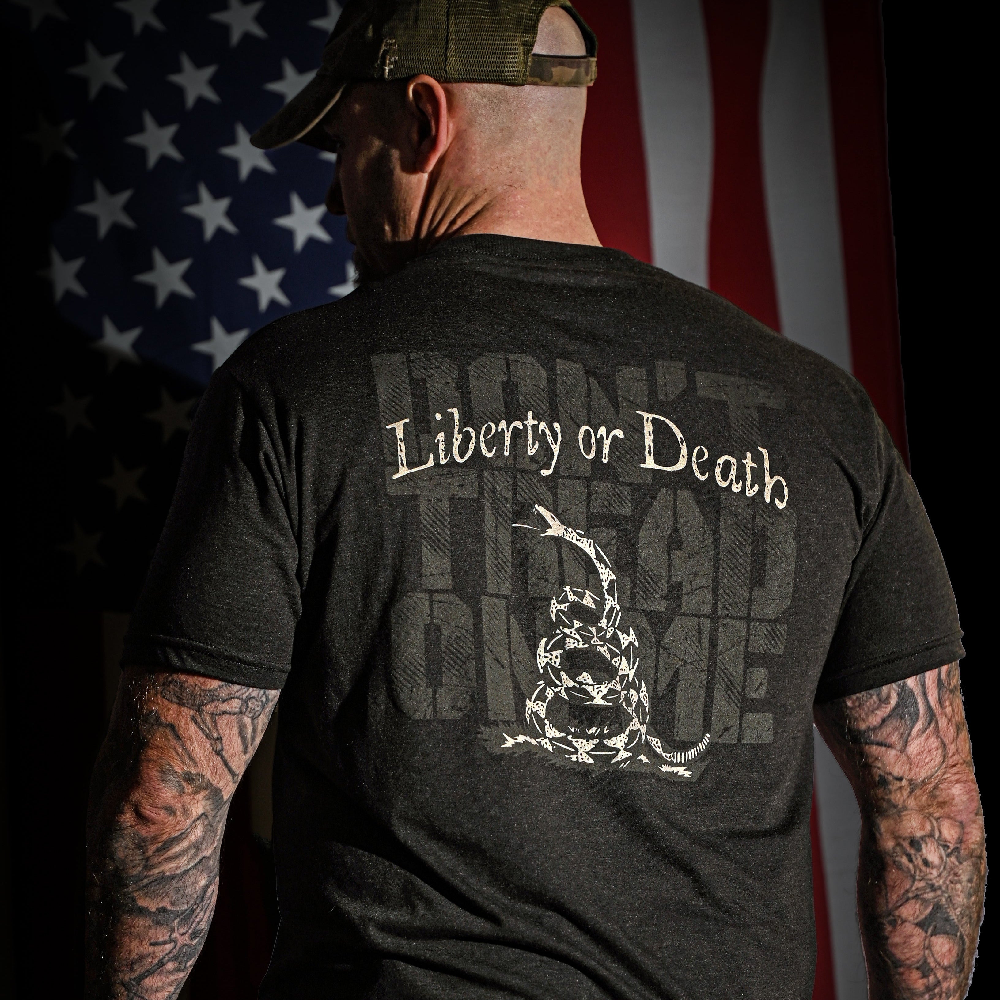 Veteran standing in front of an American flag while wearing the Liberty or Death Don't Tread on Me Tshirt
