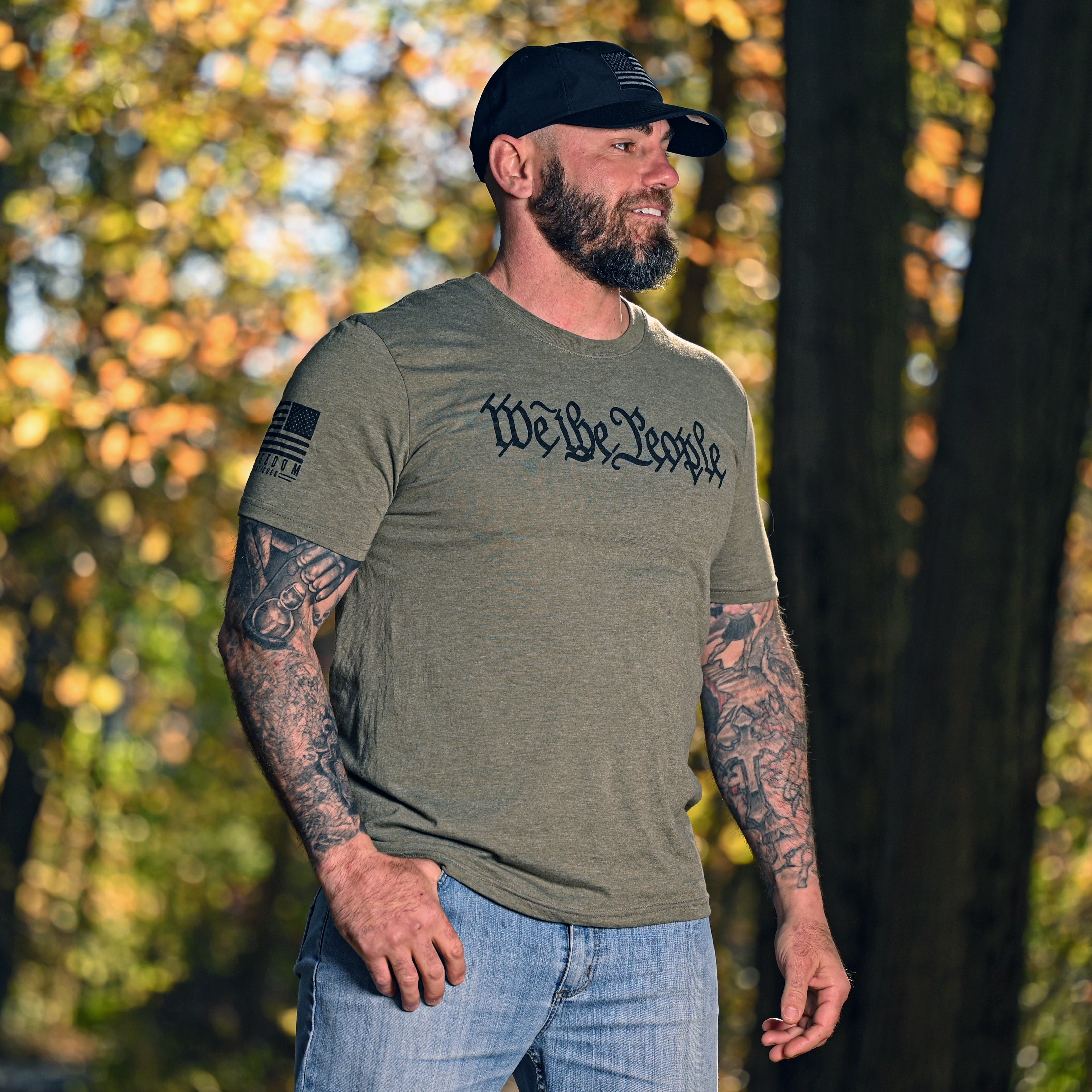 Man wearing a military green We the People t-shirt with text in a forest setting