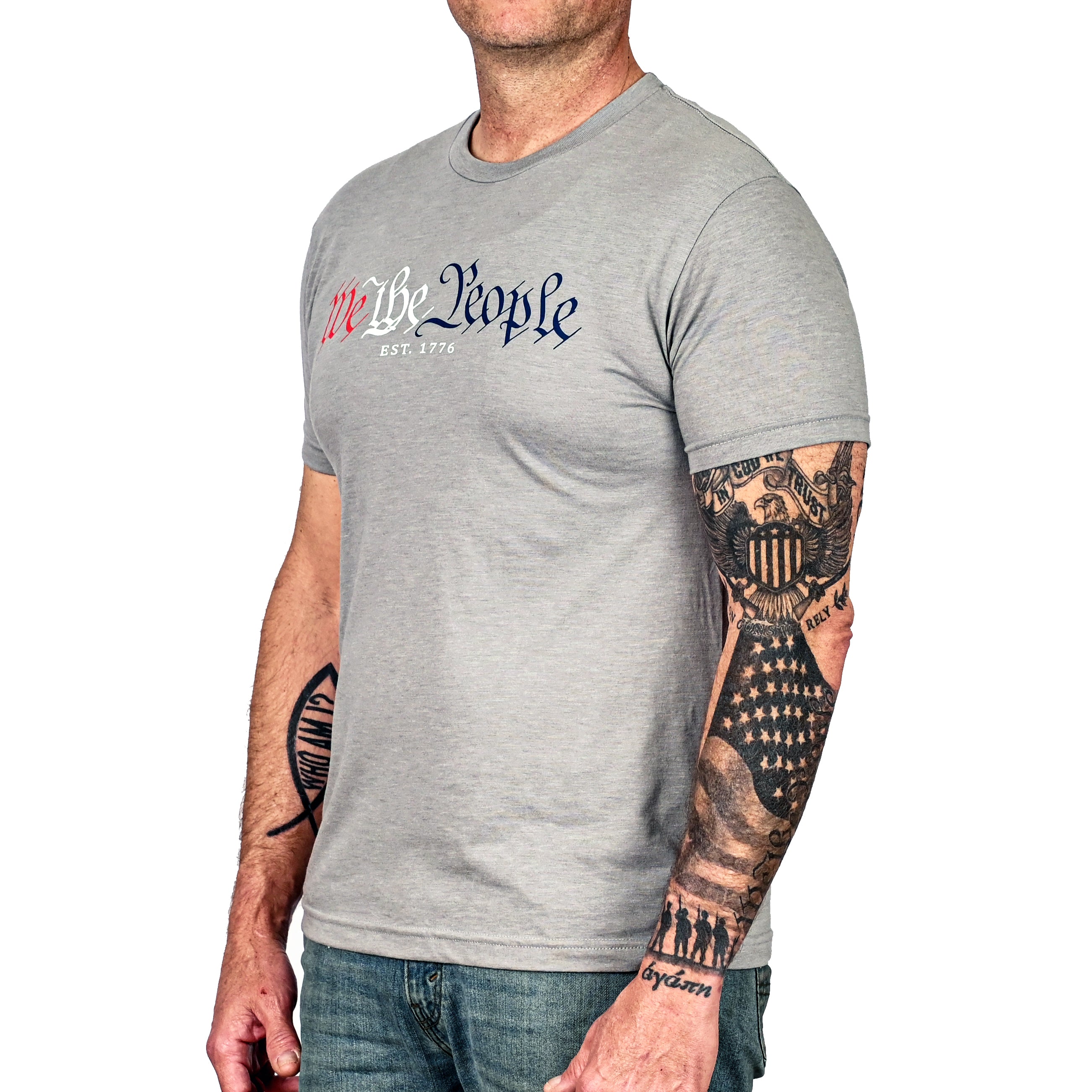 A man wearing the patriotic 'We The People' gray crew neck t-shirt with text in red and blue. (left side view)