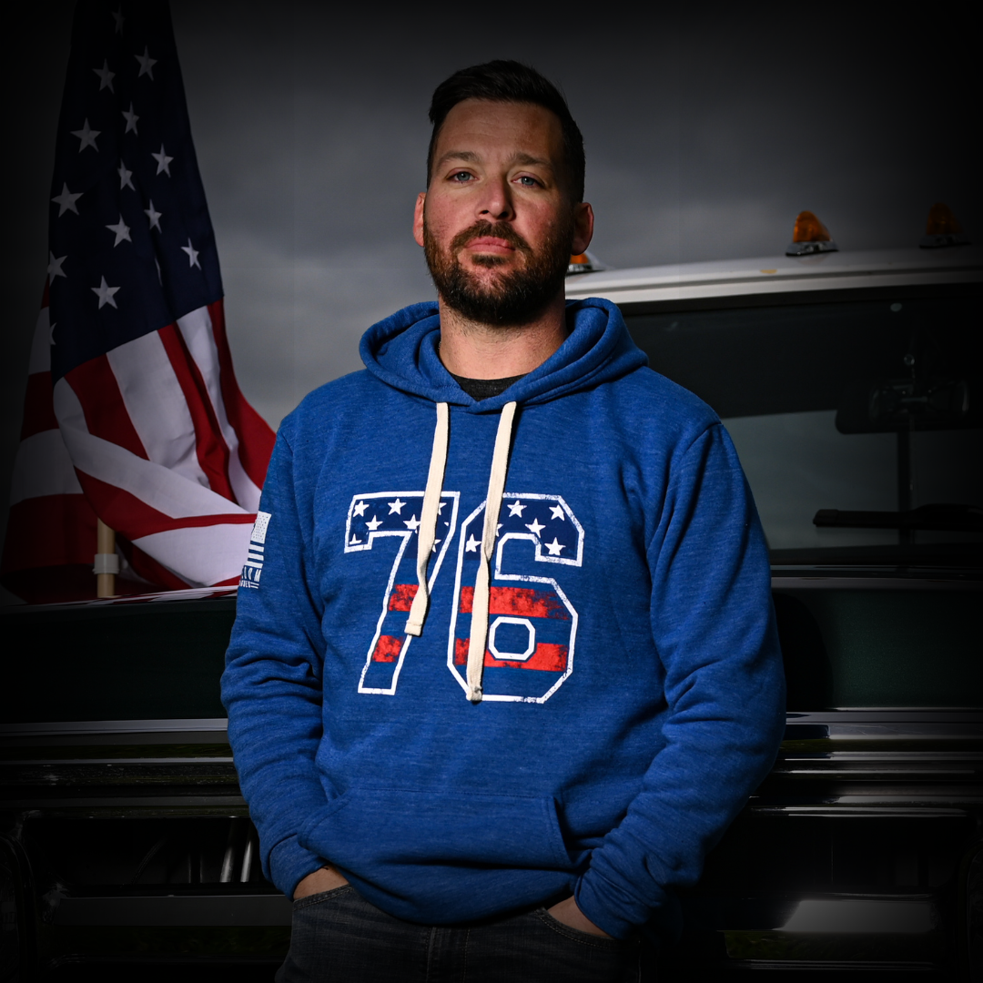Mike McKinstry wearing a blue hoodie with a 1776 design in front of an American flag