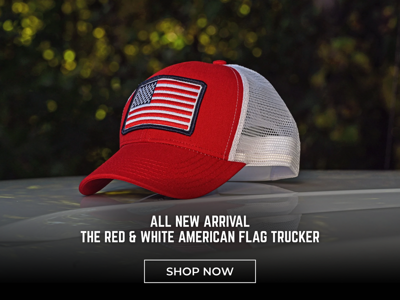 A red and white trucker cap with an American flag patch on the front, resting on a dark surface with a blurred outdoor background. Text overlay reads 'ALL NEW ARRIVAL THE RED & WHITE AMERICAN FLAG TRUCKER' with a 'SHOP NOW' button below.