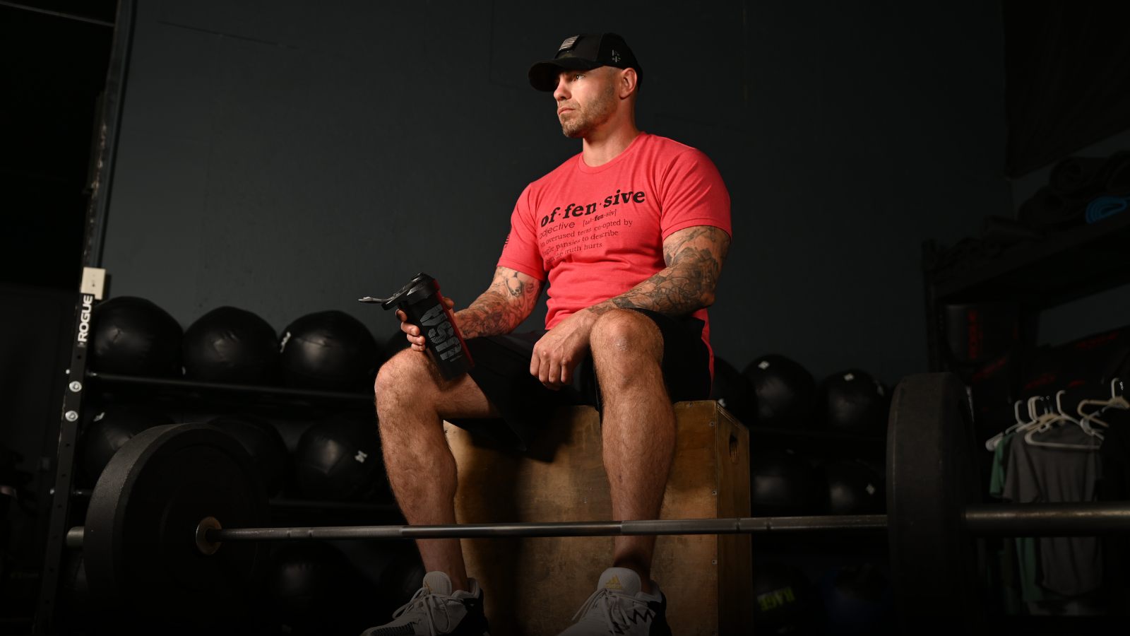 Man sitting on a weight bench holding a shaker bottle in a gym setting