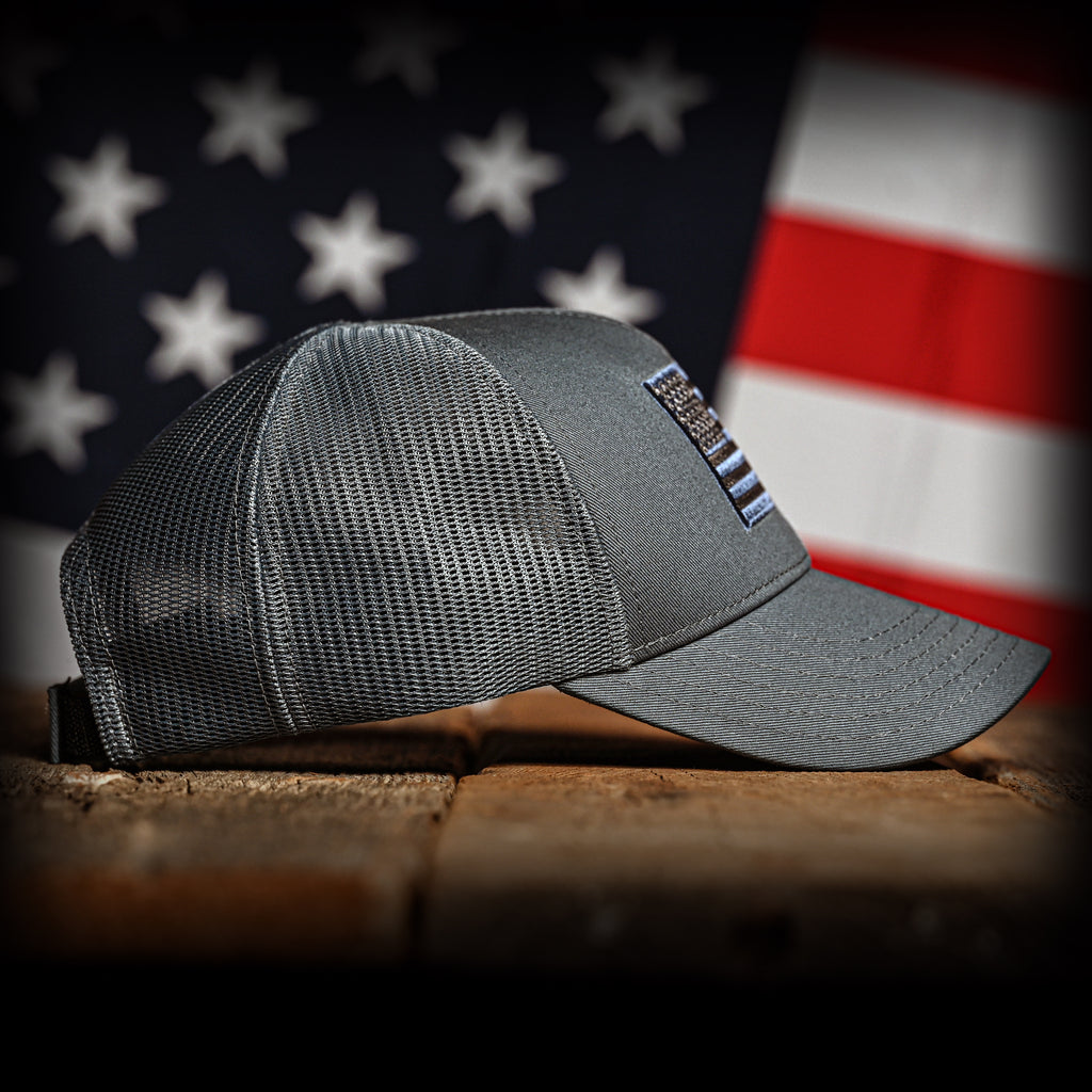 Tonal slate cap with an embroidered American flag on a wooden surface in front of an American flag, right view