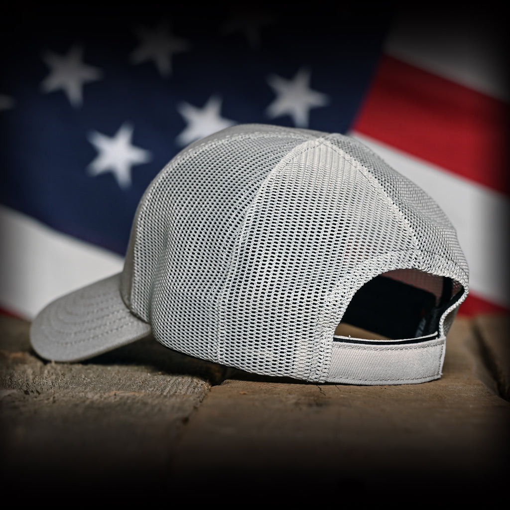 Back view of a Tonal Light Gray American Flag Hat on a wood surface against a flag backdrop 