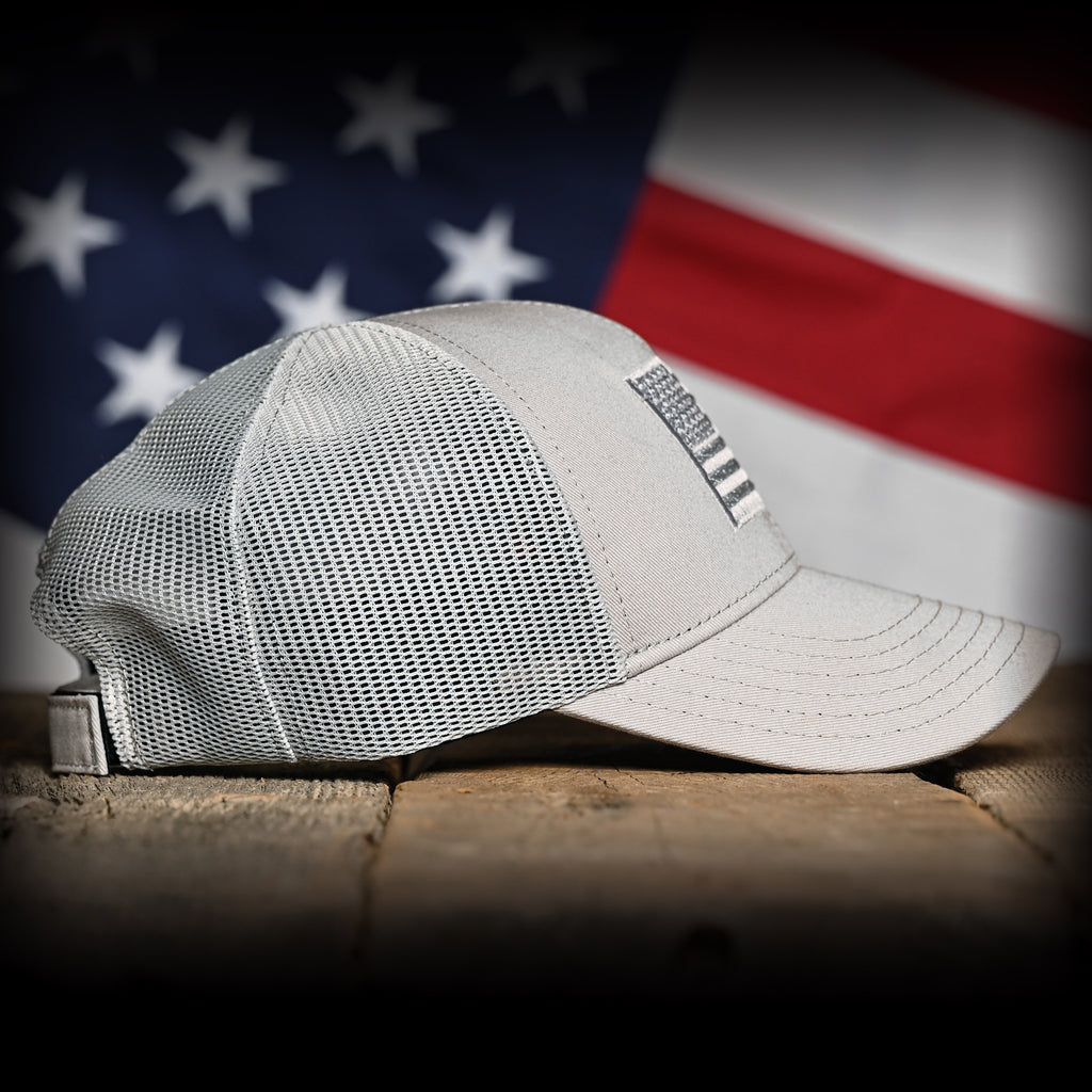 Right side of a Tonal Light Gray American Flag Hat on a wood surface against a flag backdrop 