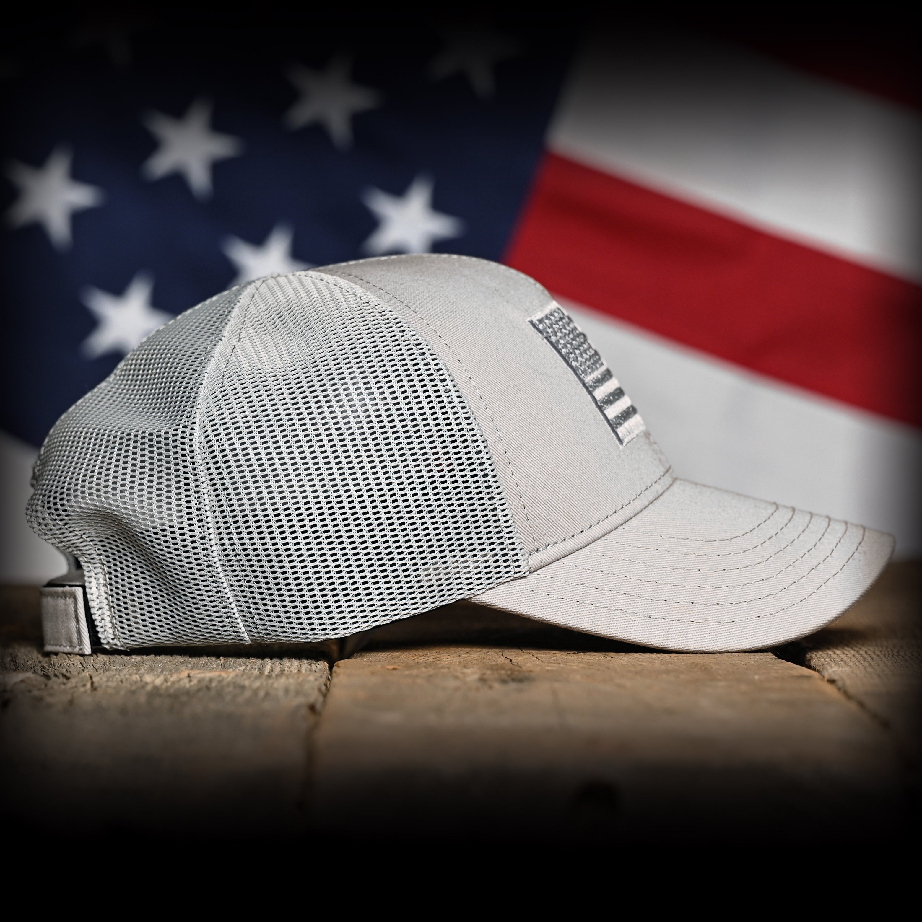 Right side of a Tonal Light Gray American Flag Hat on a wood surface against a flag backdrop 
