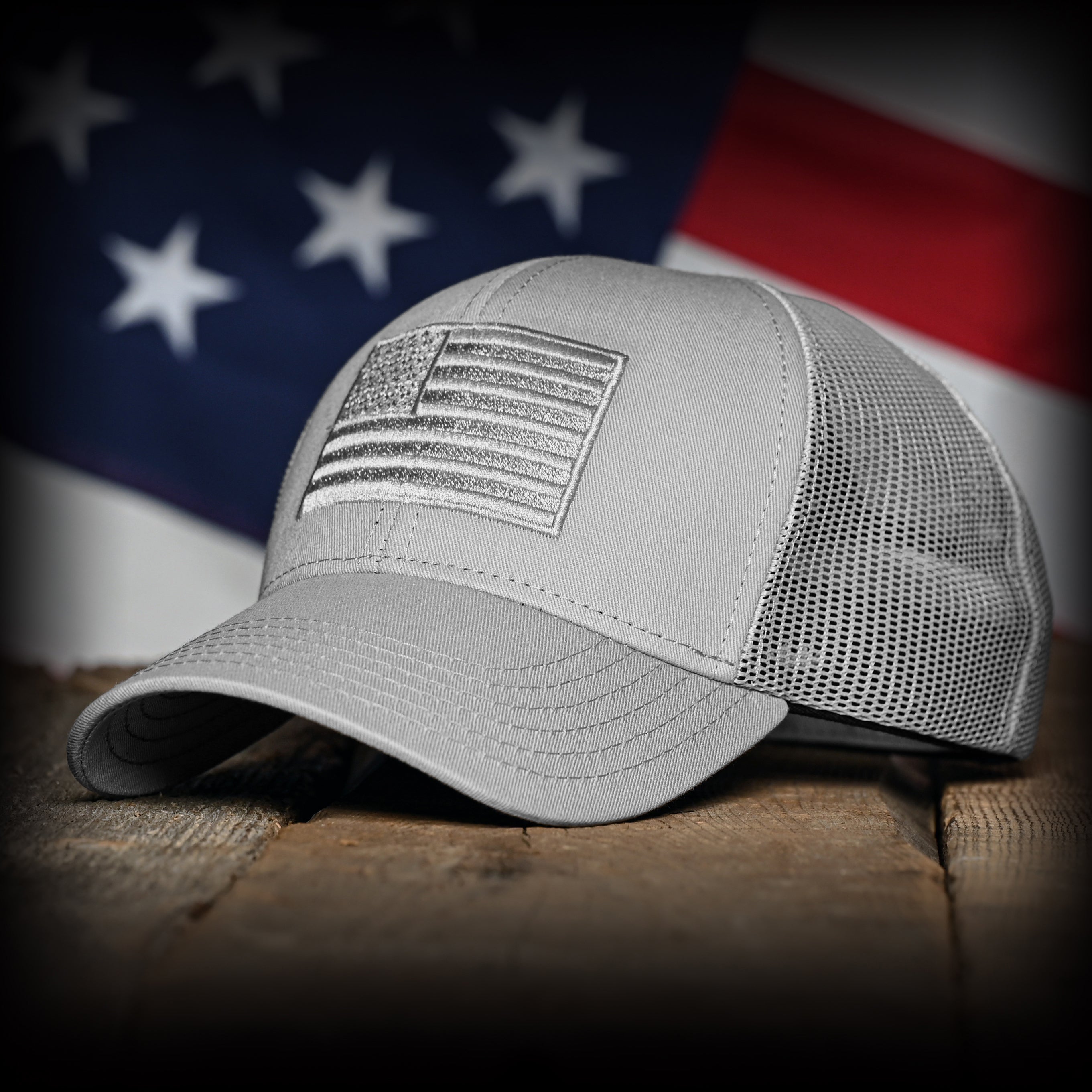 Gray cap with an embroidered American flag on a wooden surface with an American flag in the background