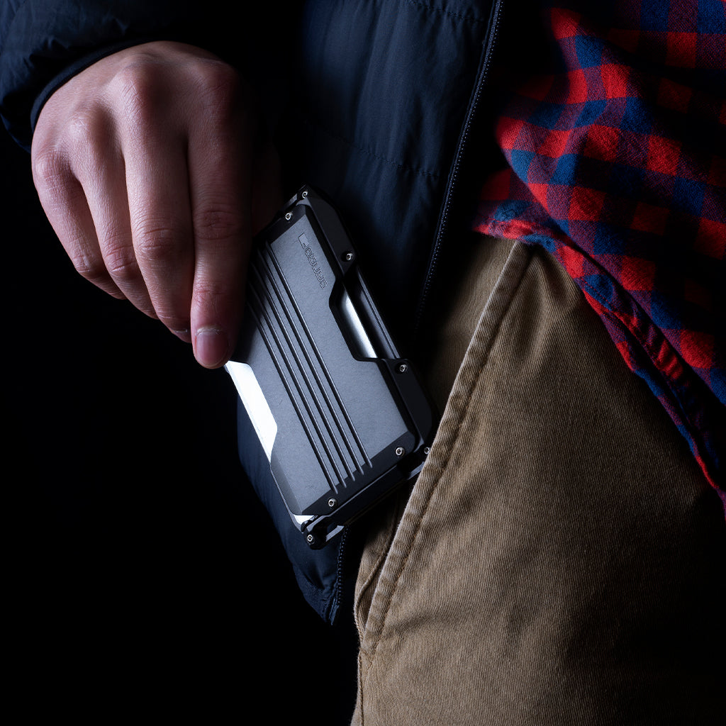 A person's hand holding a black Dango A-Series Adapt Wallet with a quick release rail mechanism.