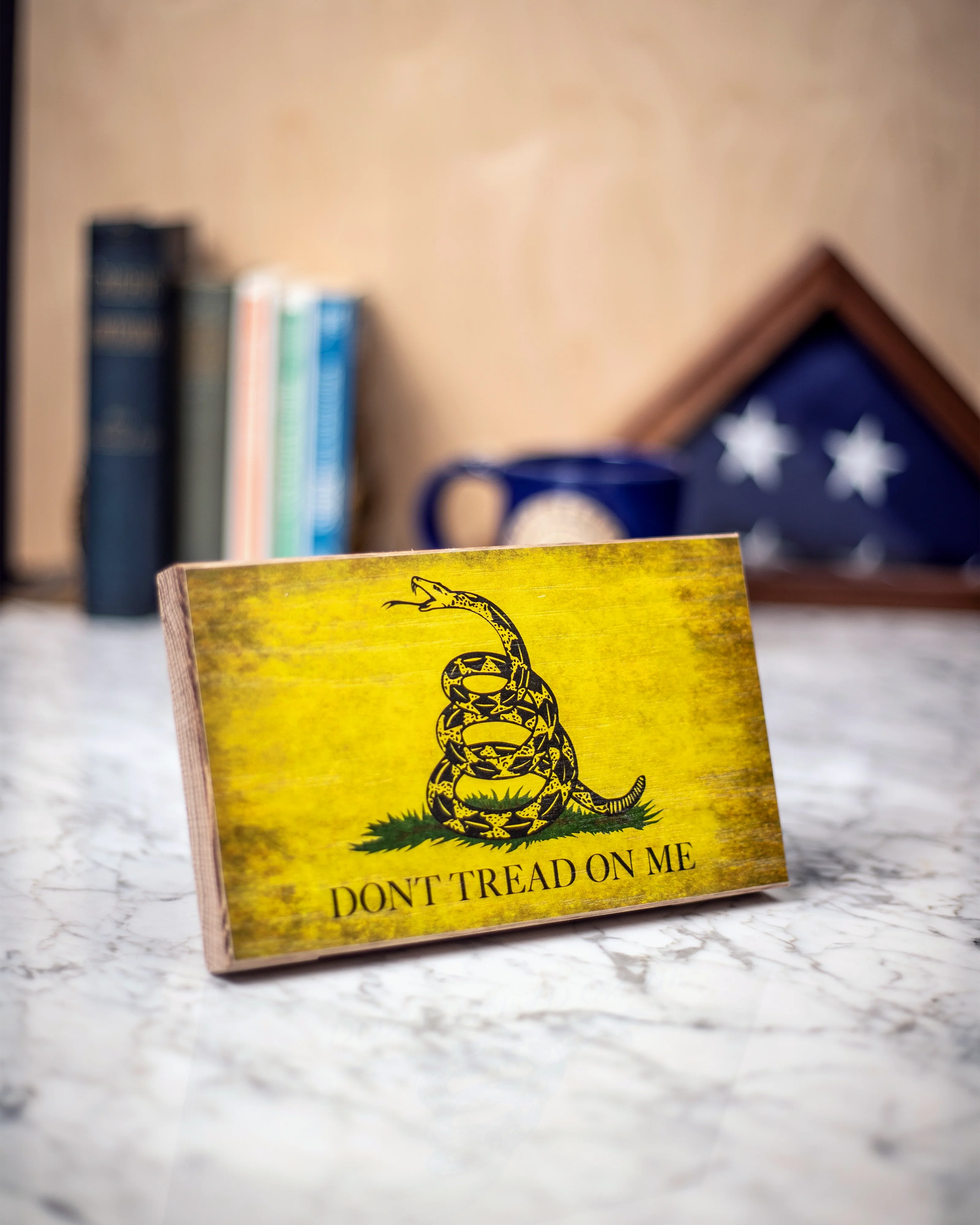 Wooden sign with 'Don't Tread on Me' design on a marble surface.