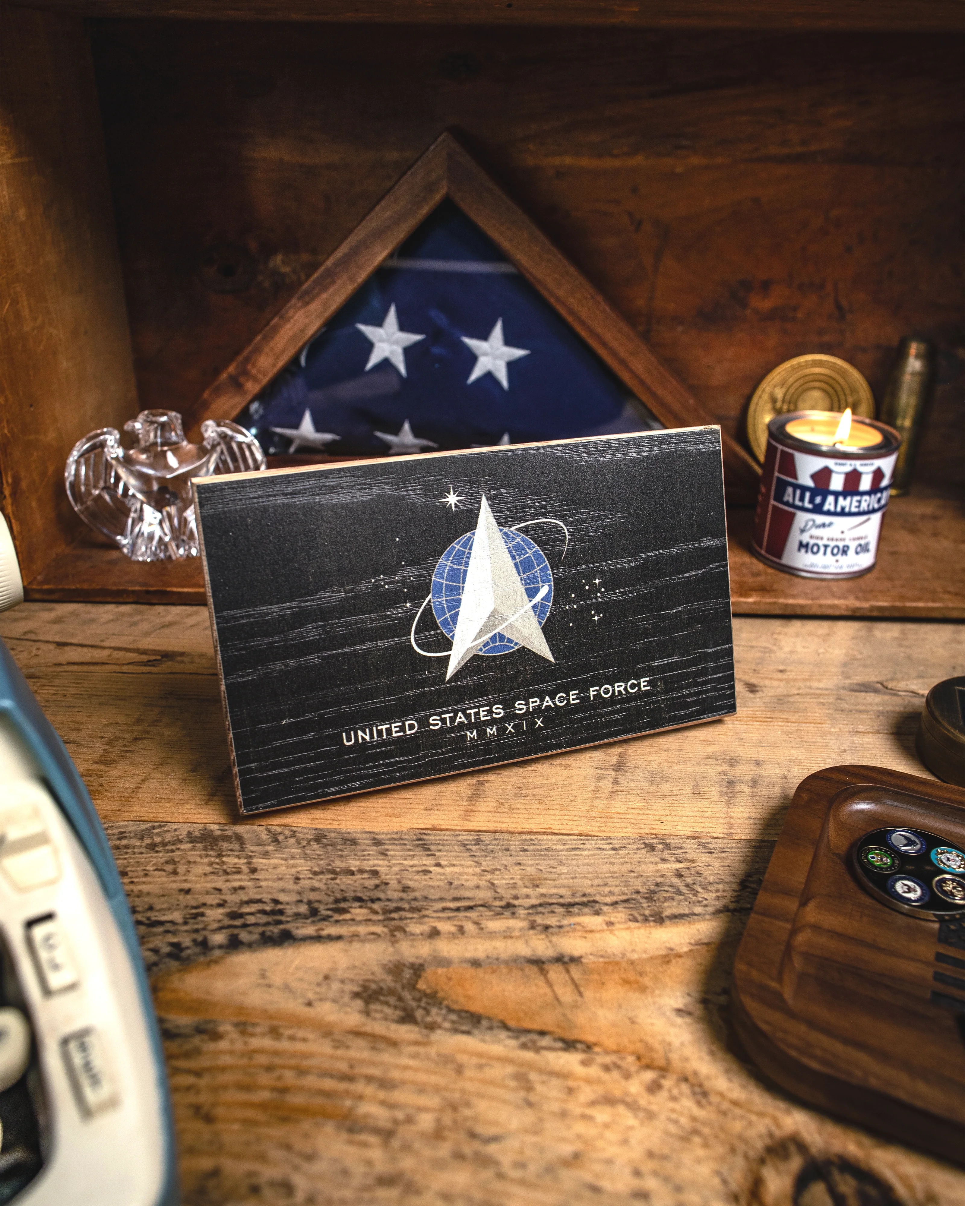 United States Space Force insignia card on a wooden surface with a flag and candle in the background